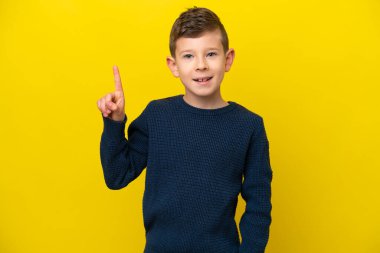 Sarı arka planda izole edilmiş beyaz çocuk harika bir fikre işaret ediyor.