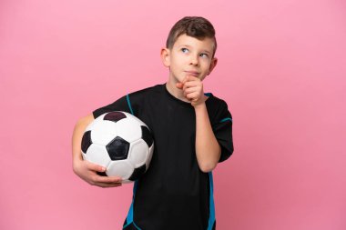 Küçük beyaz futbolcu çocuk pembe arka planda izole edilmiş ve yukarı bakıyor.
