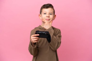Küçük beyaz çocuk pembe arka planda izole edilmiş bir bilgisayar oyunu kontrolörüyle oynuyor.