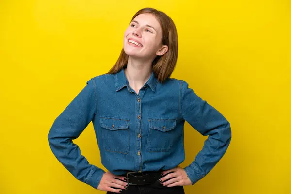 Young English woman isolated on yellow background posing with arms at hip and smiling