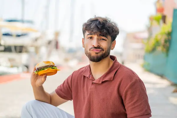 Young Arabian Handsome Man Holding Burger Outdoors Sad Expression — Stock Photo, Image