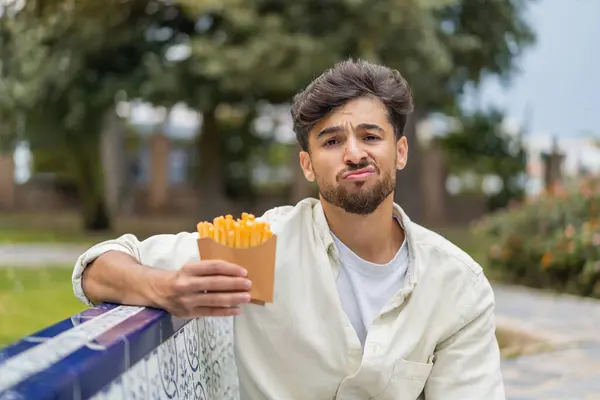 悲しい表情で屋外で揚げチップを保持している若いアラビアのハンサムな男 — ストック写真