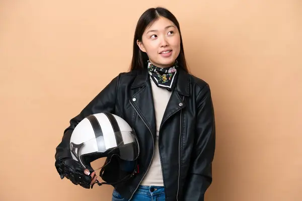 年轻的中国女人 戴着一顶米色背景的摩托车头盔 抬头一看就想出了个主意 — 图库照片