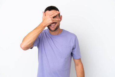 Beyaz arka planda soyutlanmış beyaz tenli yakışıklı bir adam. Gözleri elleriyle kaplıyor ve gülümsüyor.