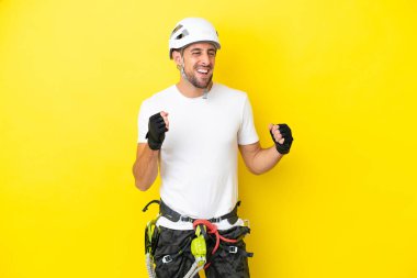 Genç kaya tırmanışçısı sarı arka planda izole edilmiş bir şekilde zaferi kutluyor.