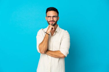 Kafkasyalı genç adam mavi arka planda izole edilmiş. Şüpheleri ve düşünceleri var.