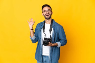 Sarı arka planda izole edilmiş genç fotoğrafçı kız mutlu bir ifadeyle selamlıyor.