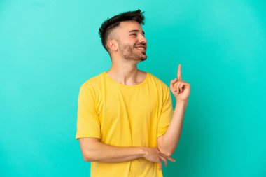 Mavi arka planda izole edilmiş genç beyaz adam harika bir fikre işaret ediyor.
