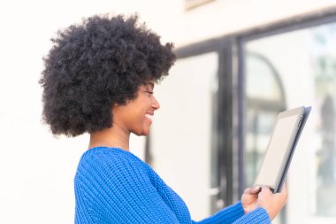 Afro-Amerikalı bir kız açık havada mutlu bir ifadeyle bir tablet tutuyor.