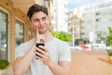 Genç yakışıklı adam cep telefonu kullanıyor ve düşünüyor.