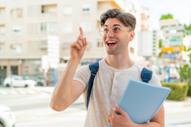 Açık havada genç ve yakışıklı bir öğrenci parmağını kaldırarak çözümü bulmaya çalışıyor.