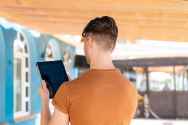 Genç yakışıklı bir adam arka tarafta tablet tutuyor.