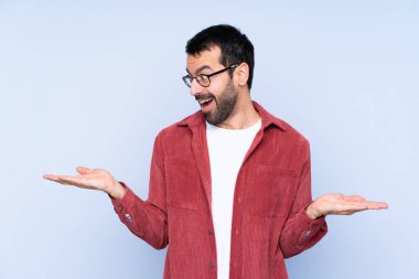 Mavi arka planda kadife ceket giyen genç beyaz adam iki eliyle kopyalama alanı tutuyor.