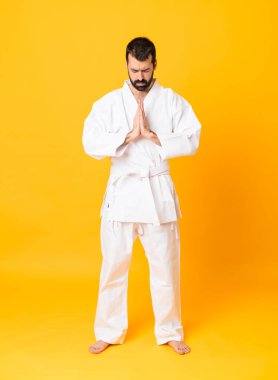 İzole edilmiş sarı arka planda karate yapan ve selam veren bir adamın tam boy fotoğrafı.