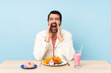 Masada kahvaltı yapan bir adam waffle yiyor ve milkshake bağırıyor ve bir şey duyuruyor.