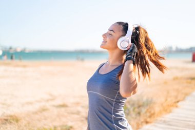 Spor giysileri giyen ve kulaklıkla müzik dinleyen genç ve güzel bir bayan.
