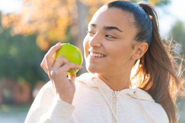 Genç, güzel, spor bir kadın elinde mutlu bir ifadeyle bir elma tutuyor.