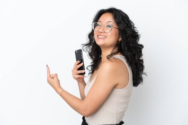 Genç Asyalı bir kadın beyaz arka planda cep telefonu kullanarak izole edilmiş.