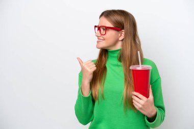 Young caucasian woman drinking soda isolated on white background pointing to the side to present a product