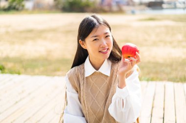 Açık havada genç bir Çinli kadın elinde mutlu bir ifadeyle bir elma tutuyor.