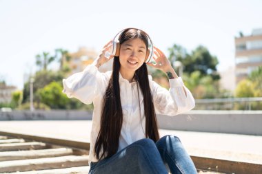 Güzel bir Çinli kadın açık havada kulaklıkla müzik dinliyor.