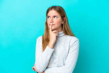 Mavi arka planda izole edilmiş genç sarışın kadın yukarı bakarken şüpheleri var.