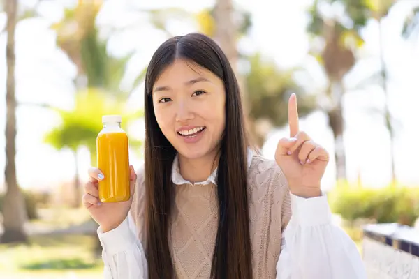 Красивая Китаянка Держит Апельсиновый Сок Открытом Воздухе Указывая Отличную Идею — стоковое фото