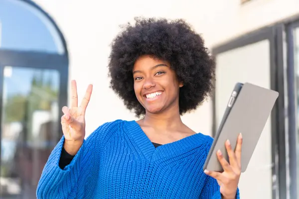African American Girl Holding Tablet Outdoors Smiling Showing Victory Sign 스톡 이미지