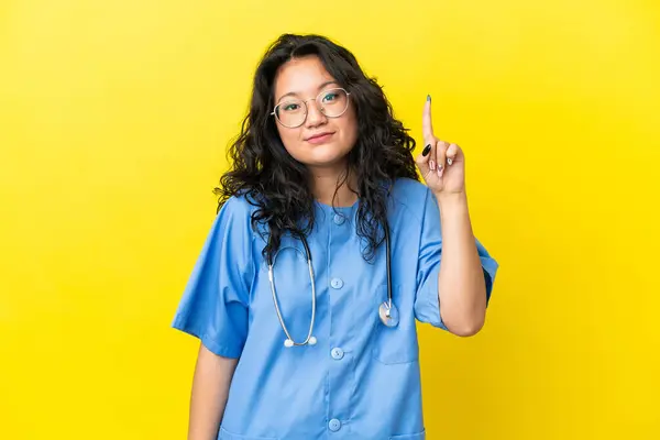 Jeune Chirurgien Médecin Asiatique Femme Isolée Sur Fond Jaune Pointant Image En Vente
