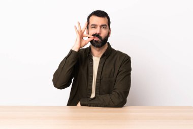 Masada sakallı beyaz bir adam sessizlik işareti gösteriyor..