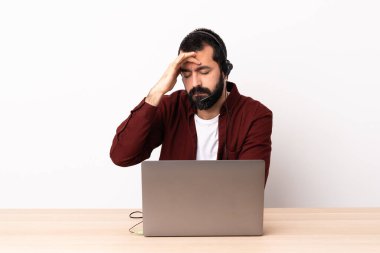 Tele pazarlamacı beyaz adam kulaklıkla ve laptopuyla baş ağrısı ile çalışıyor..