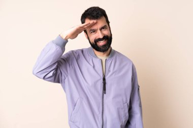 Sakallı, ceketli, soyutlanmış arka planda beyaz bir adam mutlu bir ifadeyle selam veriyor.