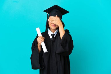 Üniversiteden mezun genç bir kız, izole edilmiş mavi arka planda, gözleri elleriyle kapatıyor.