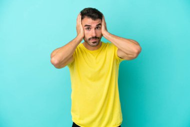 Mavi arka planda izole edilmiş genç beyaz adam gergin hareketler yapıyor.