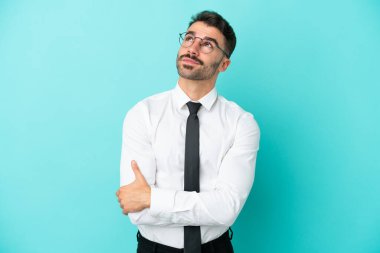Kafkasyalı iş adamı mavi arka planda izole edilmiş gülümserken yukarı bakıyor