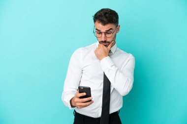 Beyaz iş adamı mavi arka planda izole edilmiş düşünüyor ve bir mesaj gönderiyor.