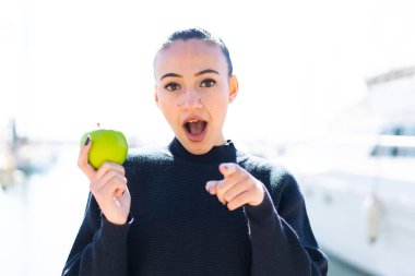Açık havada elmalı genç Faslı kız şaşırmış ve ön tarafı işaret ediyor.