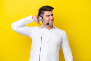 Tele pazarlamacı beyaz adam sarı arka planda, boyunluk takan kulaklıkla çalışıyor.