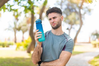 Genç yakışıklı sporcu, dışarıda bir şişe suyla üzgün bir ifadeyle.
