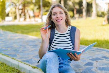 Açık havada elinde bir defter tutan sarışın genç bir kadın.