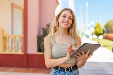Açık havada genç sarışın kadın tablet ekranına mutlu bir ifadeyle dokunuyor.