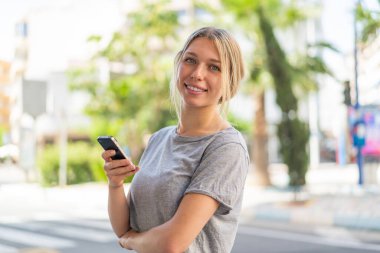 Dışarıda cep telefonu tutan ve kolları bağlı genç sarışın bir kadın.