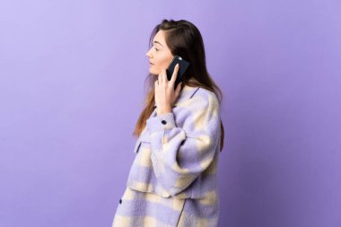 Mor arka planda izole edilmiş genç İrlandalı bir kadın cep telefonuyla sohbet ediyor.