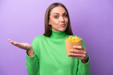 Mor arka planda kızarmış patates kızartması tutan genç beyaz kadın ellerini kaldırırken şüpheye düşüyor.