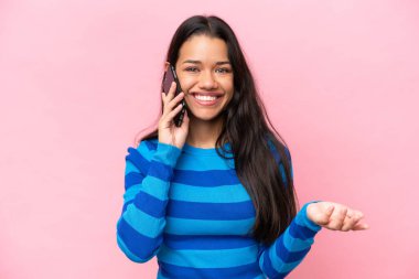 Young Colombian woman isolated on pink background keeping a conversation with the mobile phone with someone