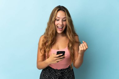 Mavi arka planda izole edilmiş genç sarışın kadın şaşırdı ve bir mesaj gönderiyor.