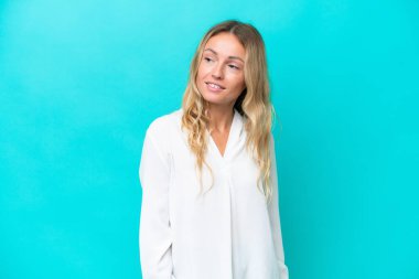 Genç Rus kadın mavi arka planda izole edilmiş, yan tarafa bakıyor ve gülümsüyor.