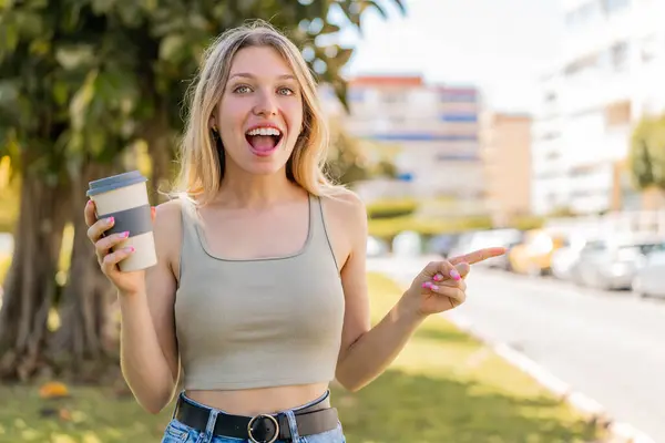 Young Blonde Woman Holding Take Away Coffee Outdoors Surprised Pointing Stock Photo