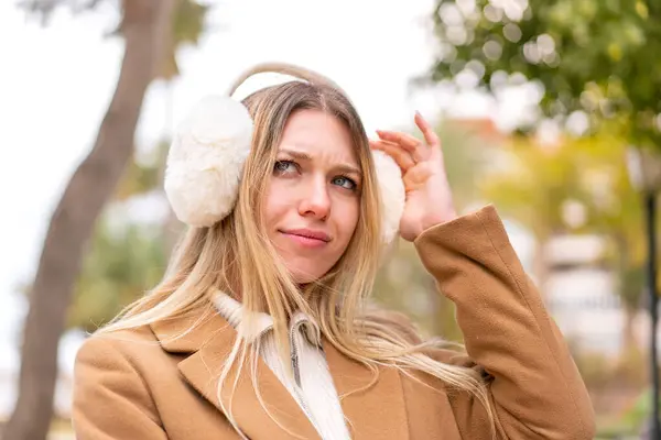 年轻漂亮的金发女人穿着冬季的围巾在户外有疑问 免版税图库照片