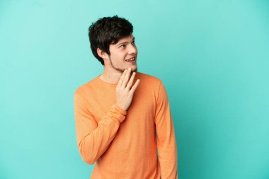 Genç Rus adam mavi arka planda izole edilmiş gülümserken yukarı bakıyor.